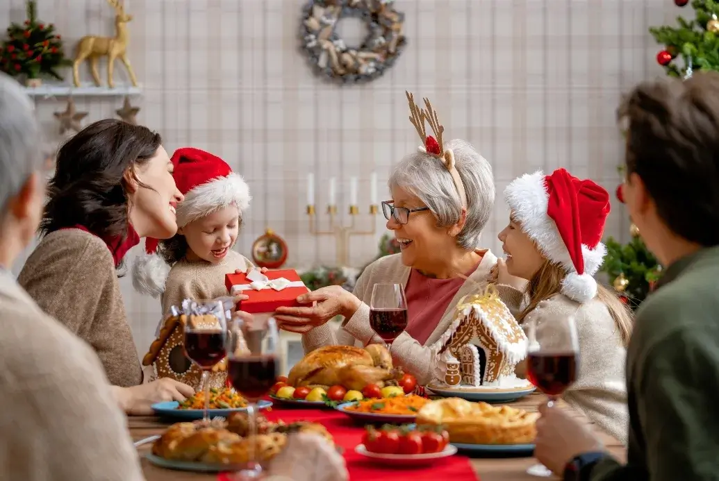 Family gathered around a festive holiday table exchanging gifts and enjoying a joyful Christmas meal